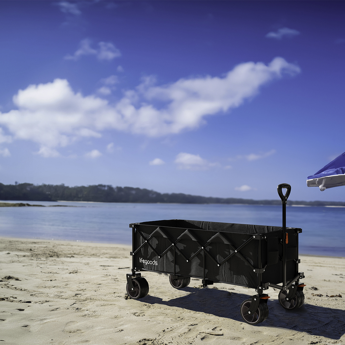 A black beach wagon sits on the sand by the sea under a blue sky.