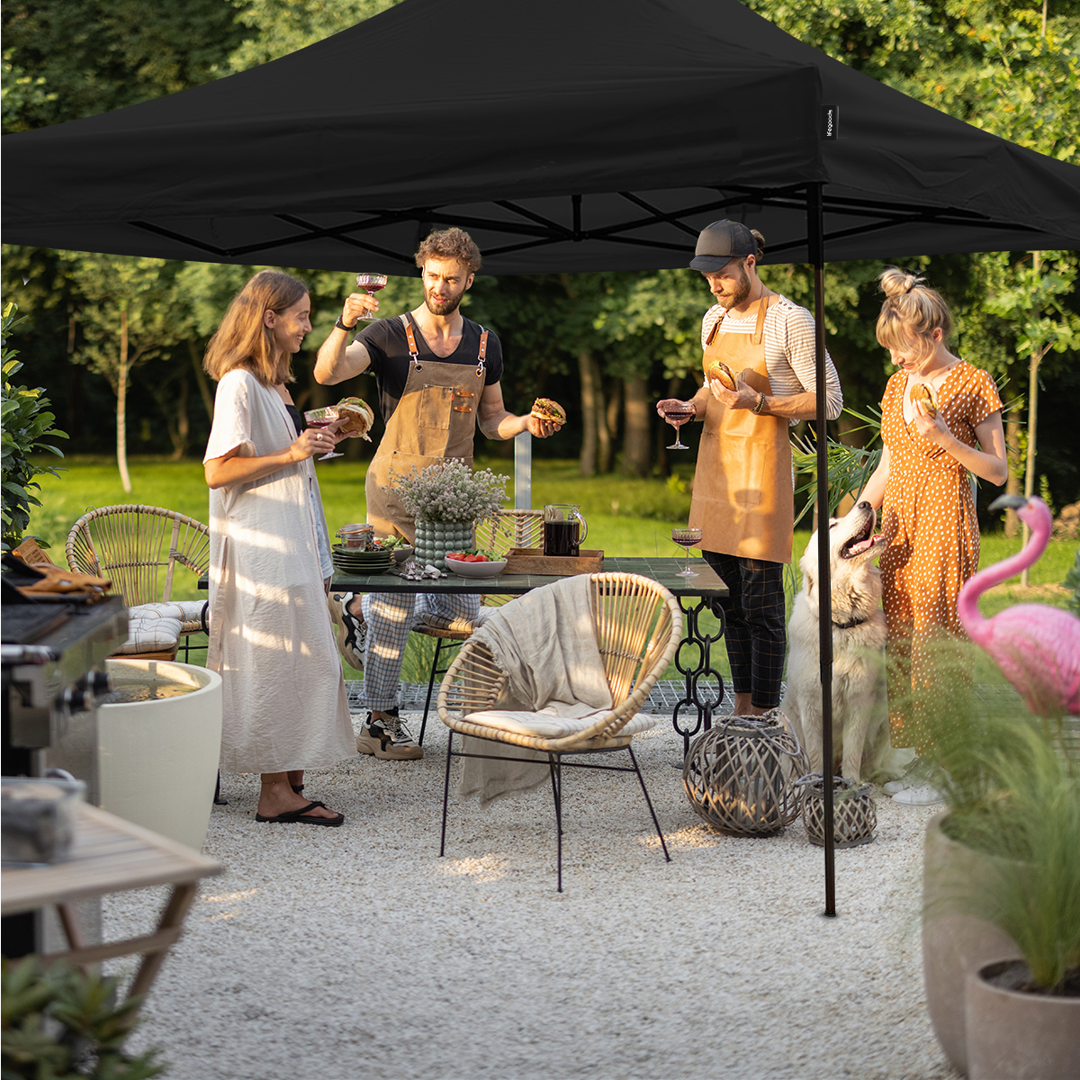 People socialize under a black canopy with food and drinks; a dog sits nearby.