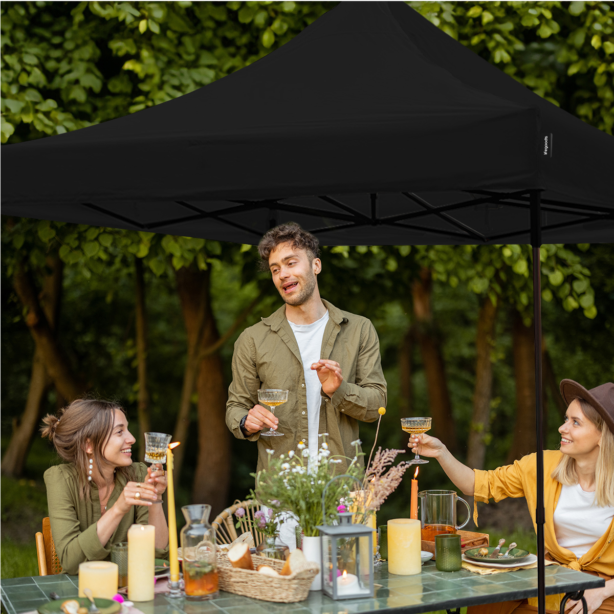 People toasting under a black canopy outdoors at a table set for a meal.