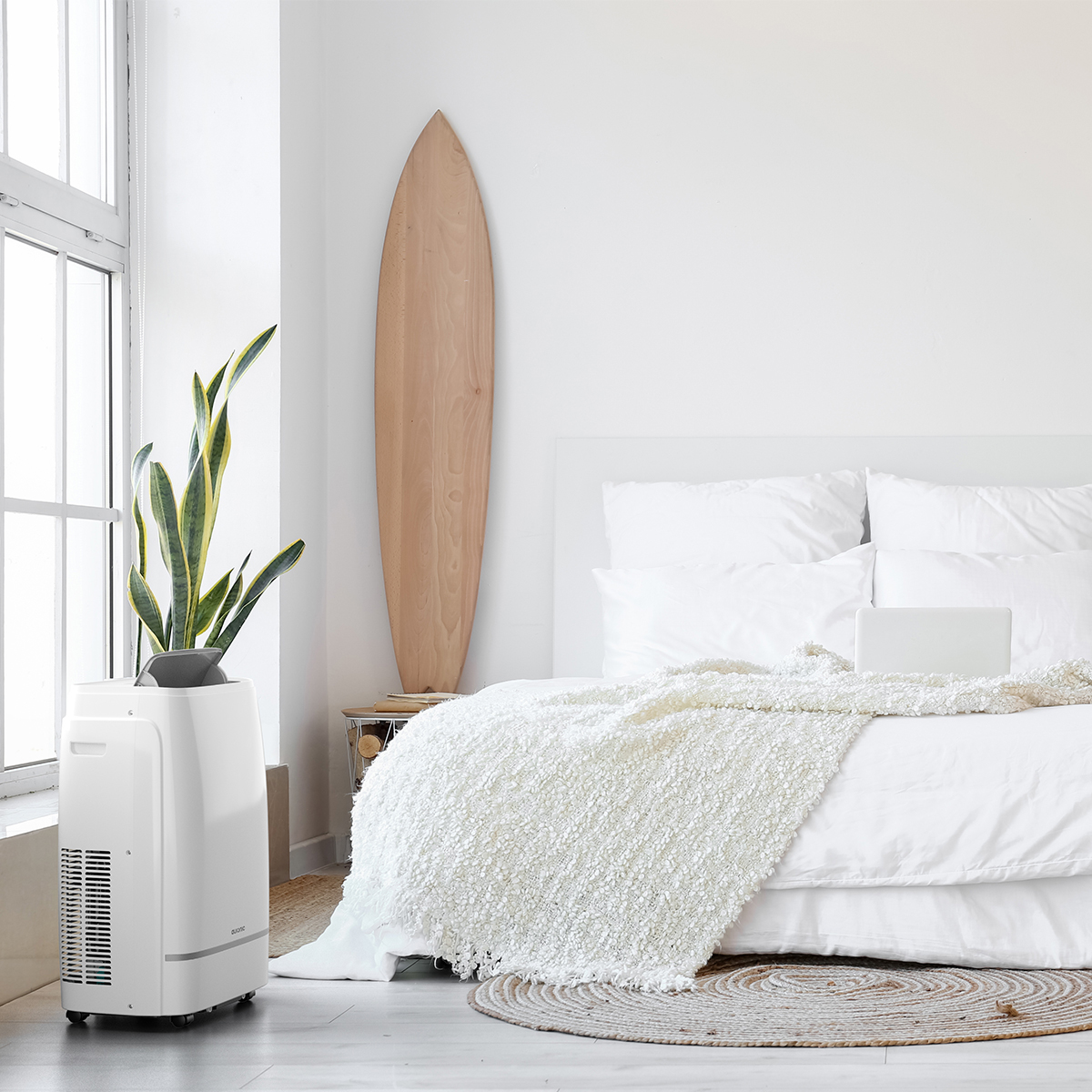 Un rafraîchisseur d'air blanc à côté d'un lit avec des oreillers blancs et une couverture.