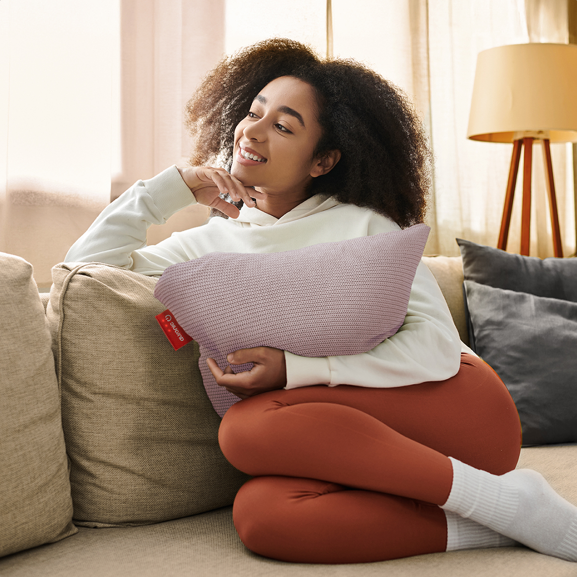 A woman sits on a sofa, holding a pillow.