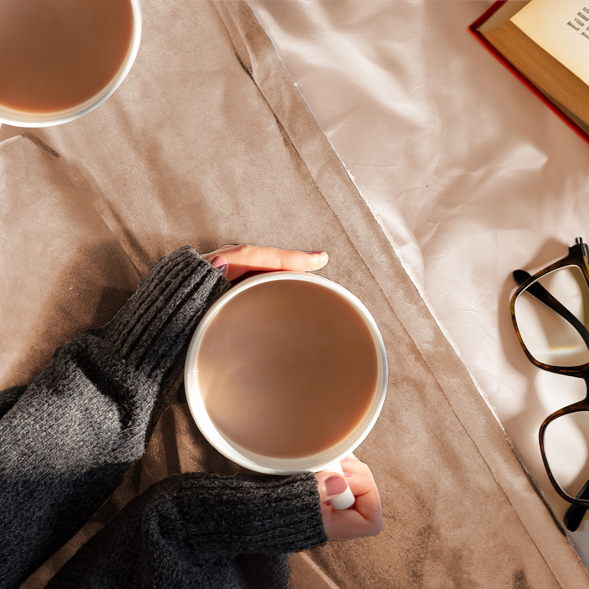 Hands hold a mug of cocoa next to a book and glasses.