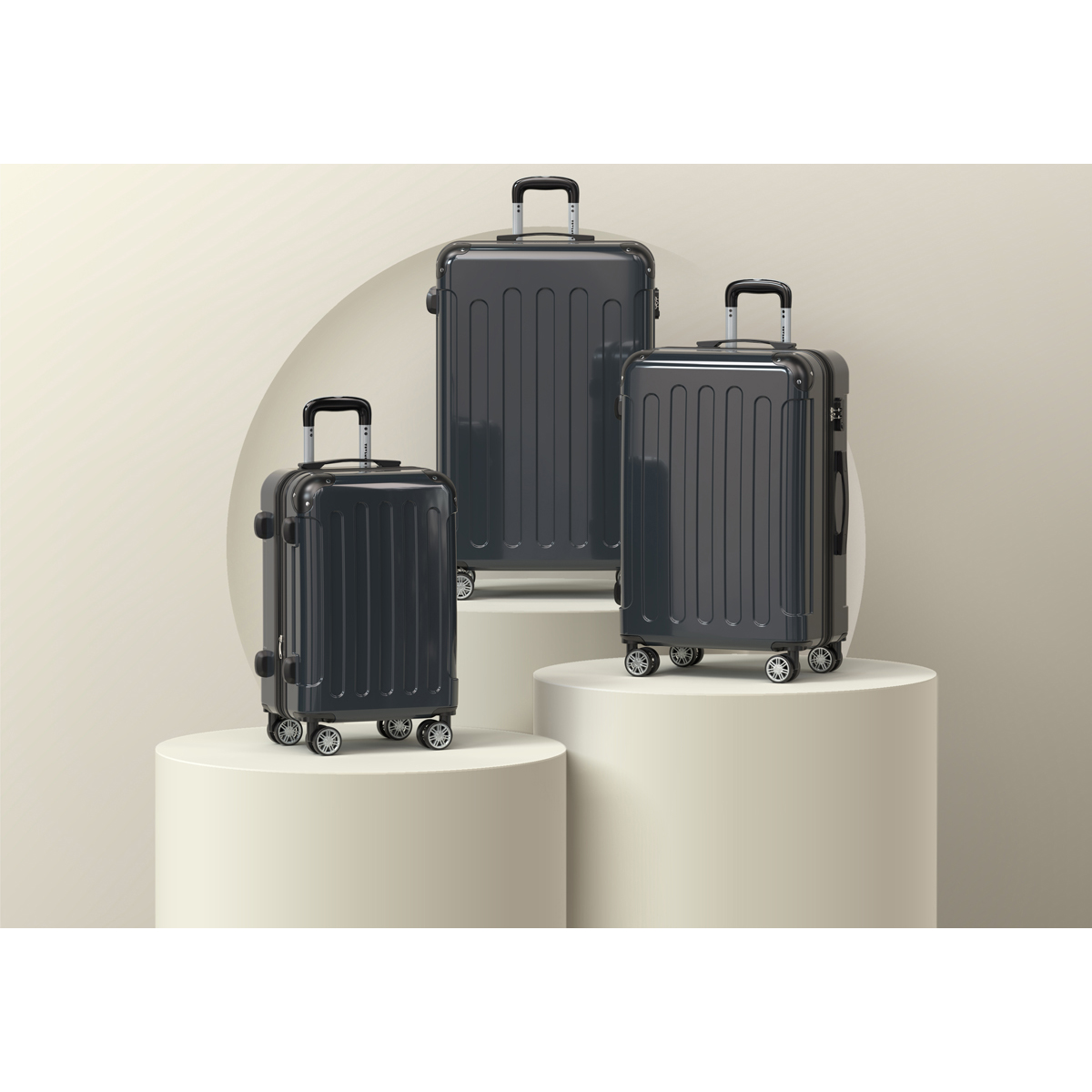 Three dark grey suitcases of varying sizes displayed on pedestals.