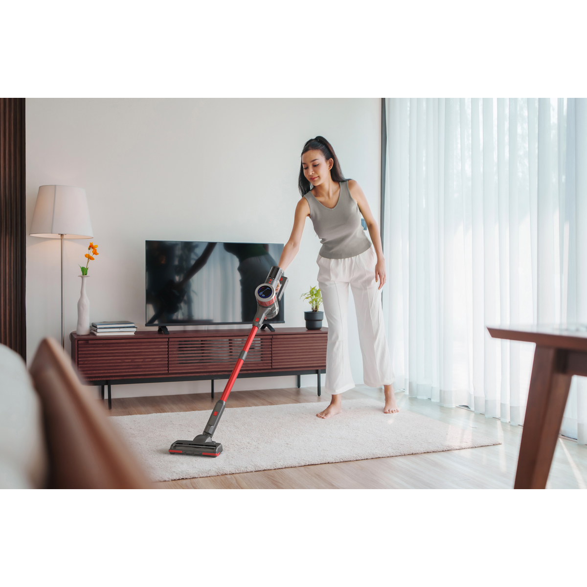 Une femme passe l'aspirateur sur un tapis avec un aspirateur rouge et gris.