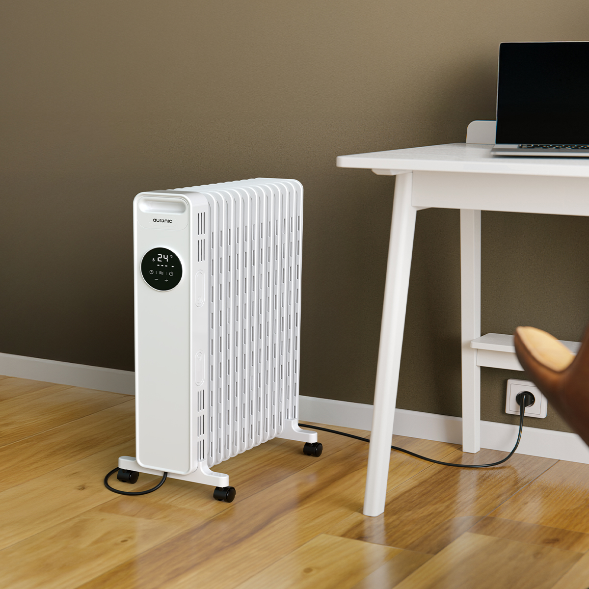 Ein weißer Ölradiator steht neben einem weißen Schreibtisch mit Laptop.