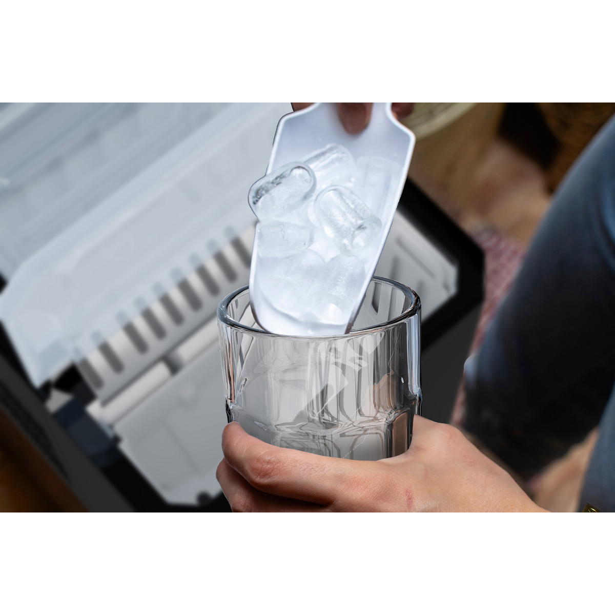 A hand pours ice from a scoop into a glass near an ice maker.