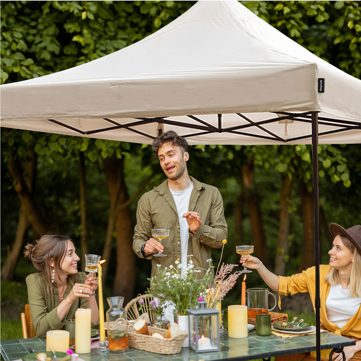 Three people sit under a gazebo at a table with food and drinks.