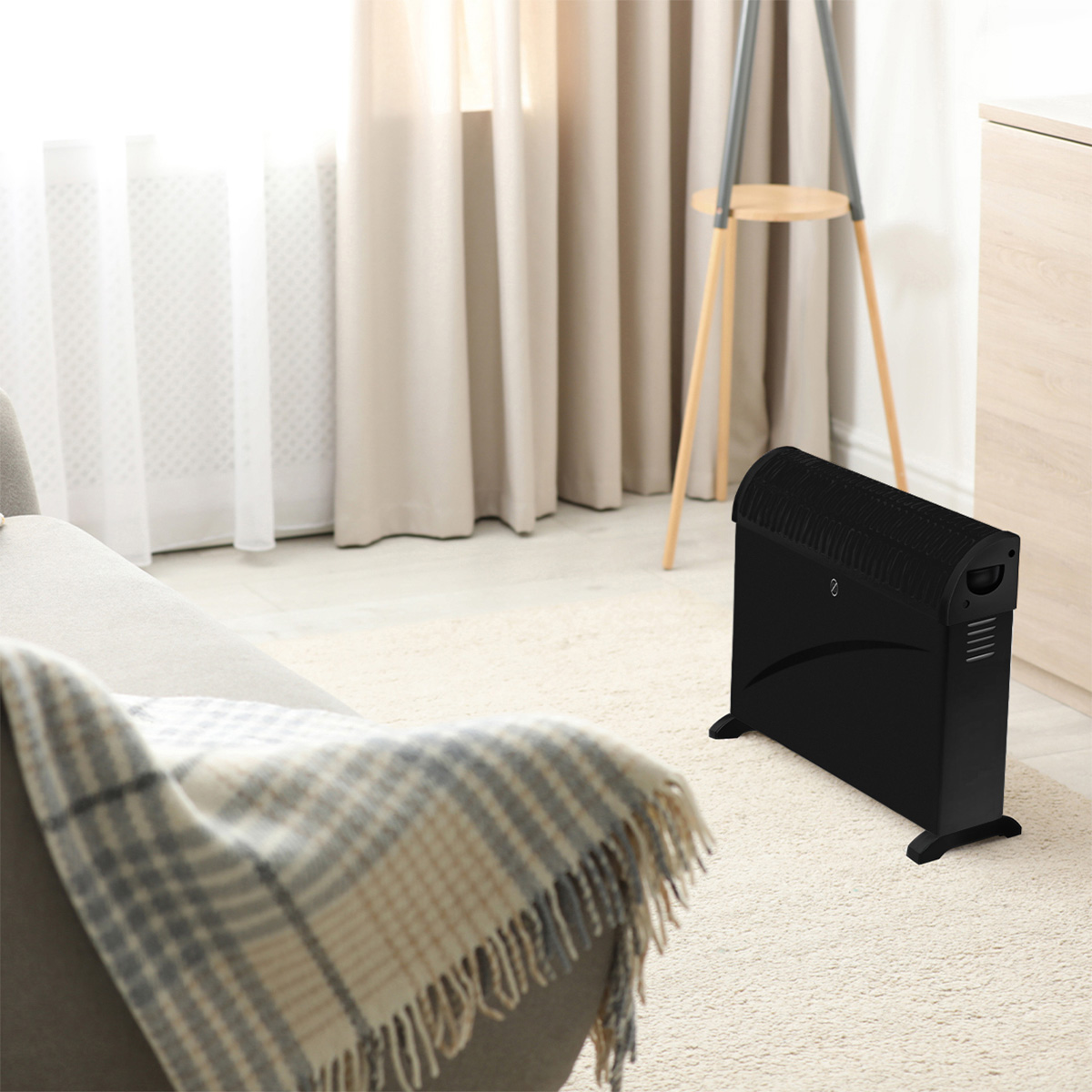 A black electric heater stands on a cream rug in a room with a sofa and curtains.