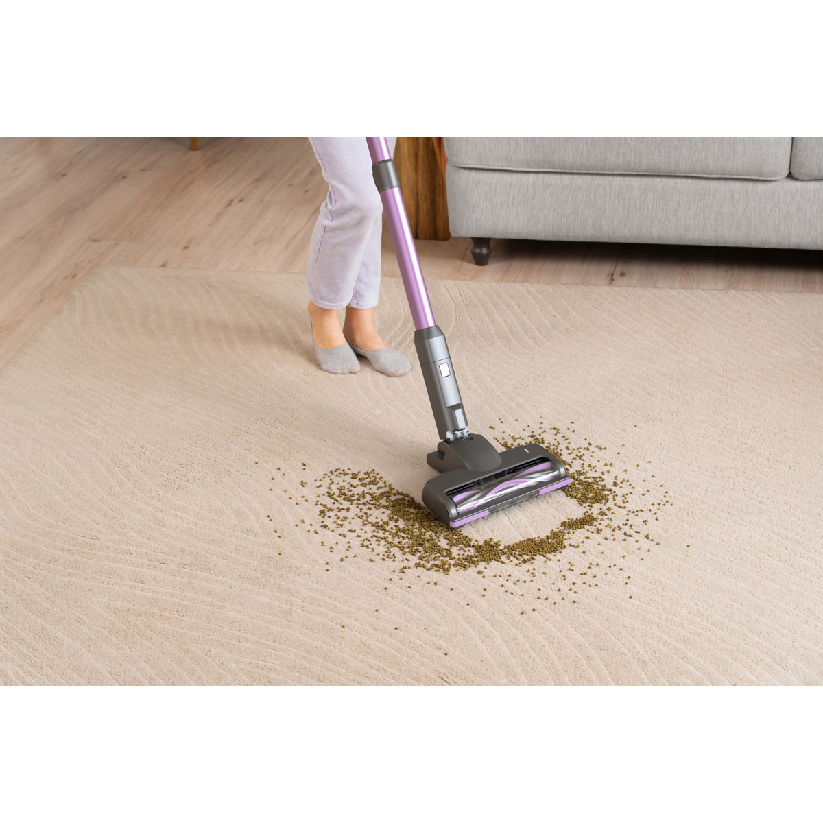Une personne passe l'aspirateur sur des haricots verts sur un tapis beige clair avec un aspirateur violet.
