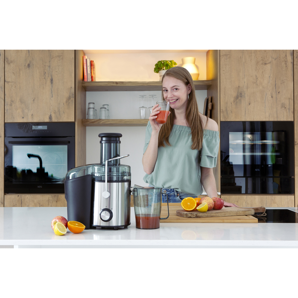 Eine Frau trinkt frisch gepressten Saft neben einer Saftpresse und Obst.