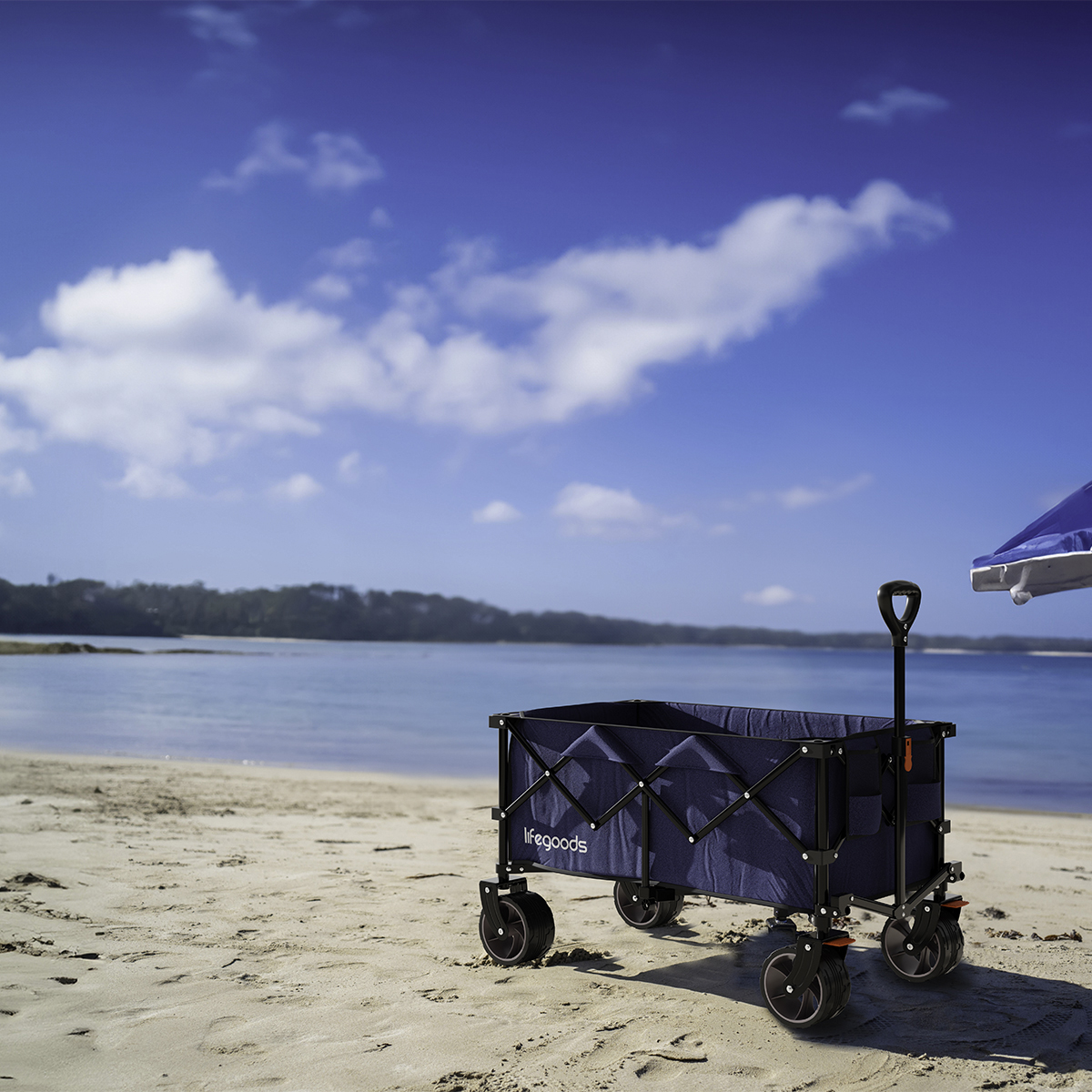 A blue beach wagon sits on a sandy beach beside the sea under a blue sky with clouds.