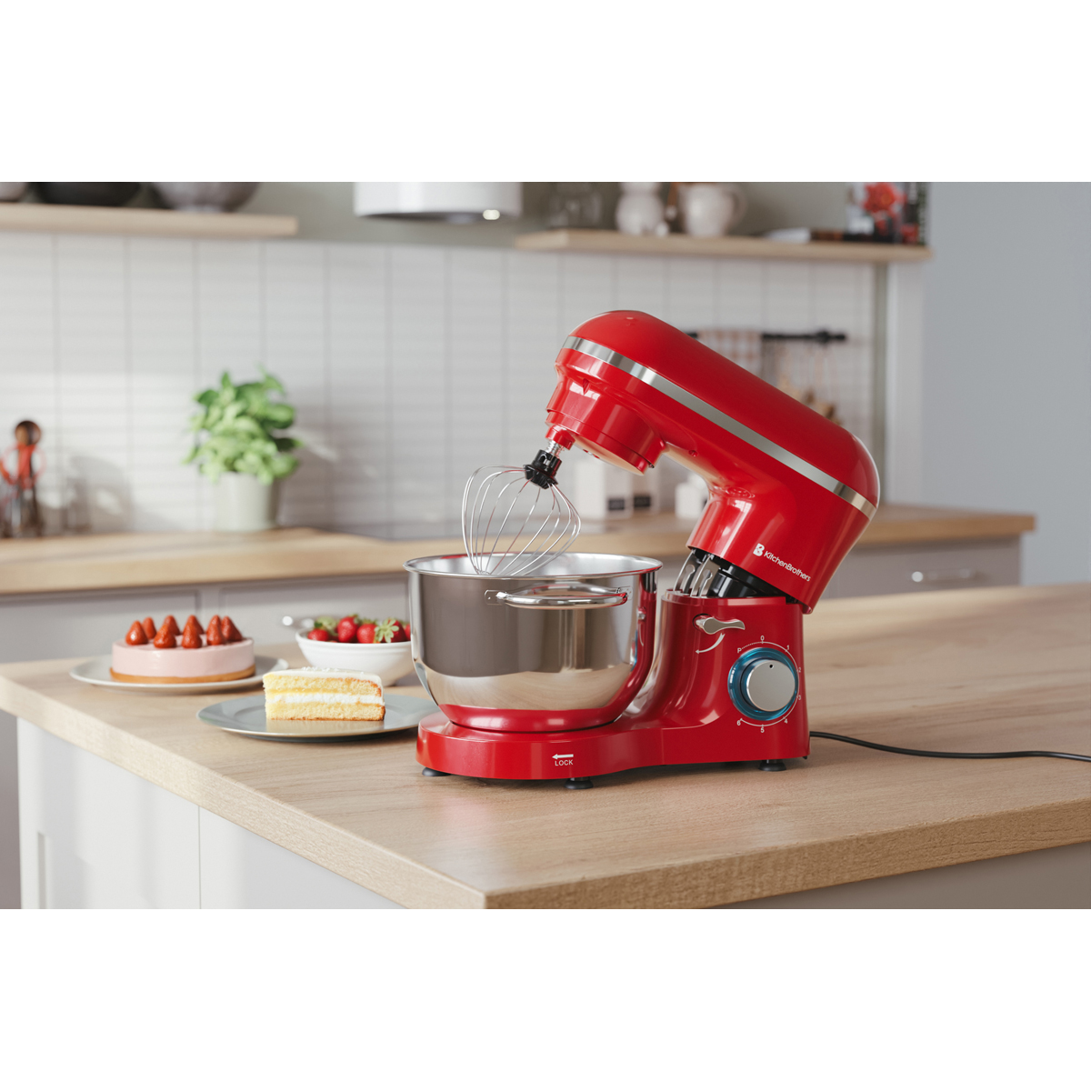 Un robot pâtissier rouge avec fouet est sur un comptoir en bois à côté d'un gâteau et de fraises.