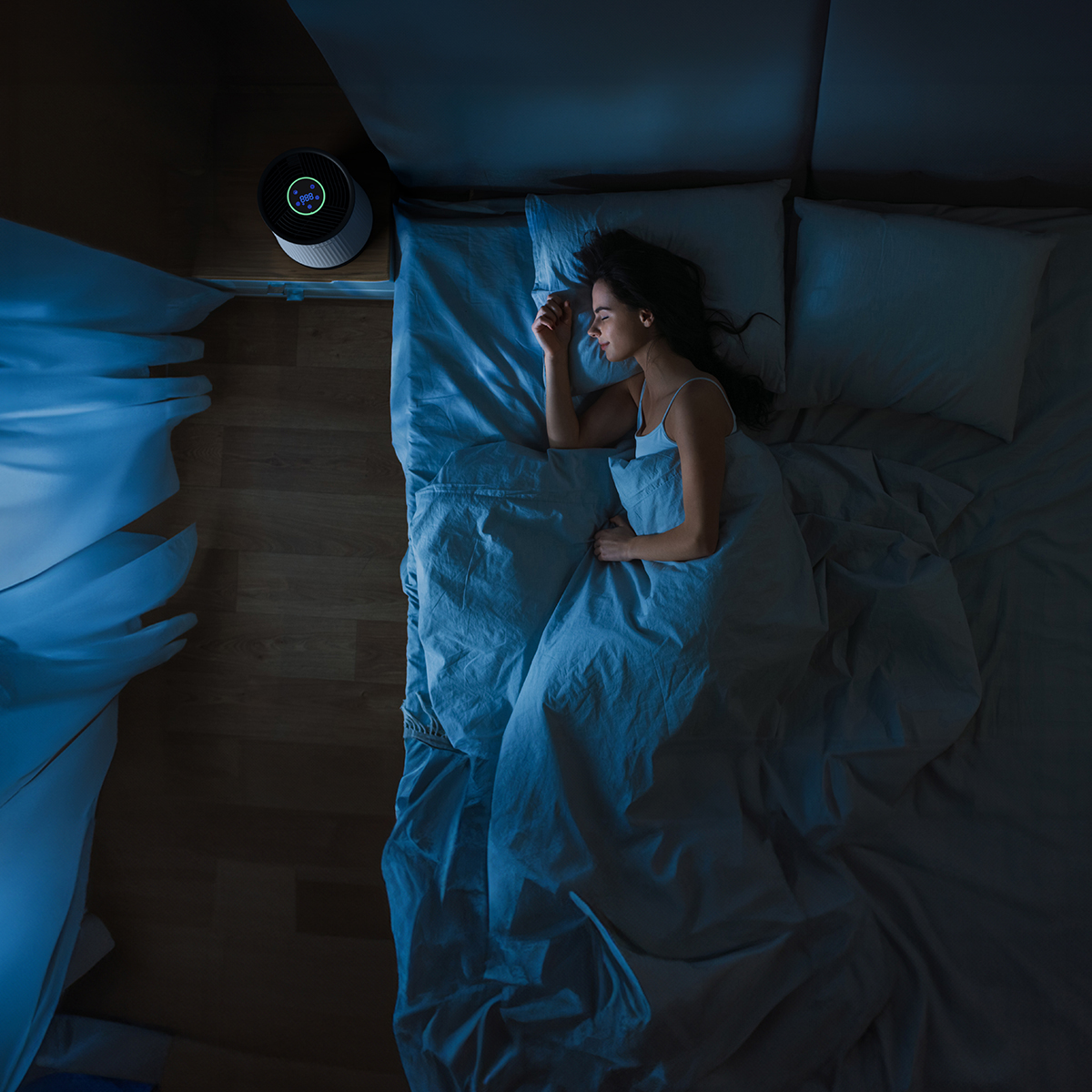 A woman sleeps in bed in the dark, an air purifier on nightstand.