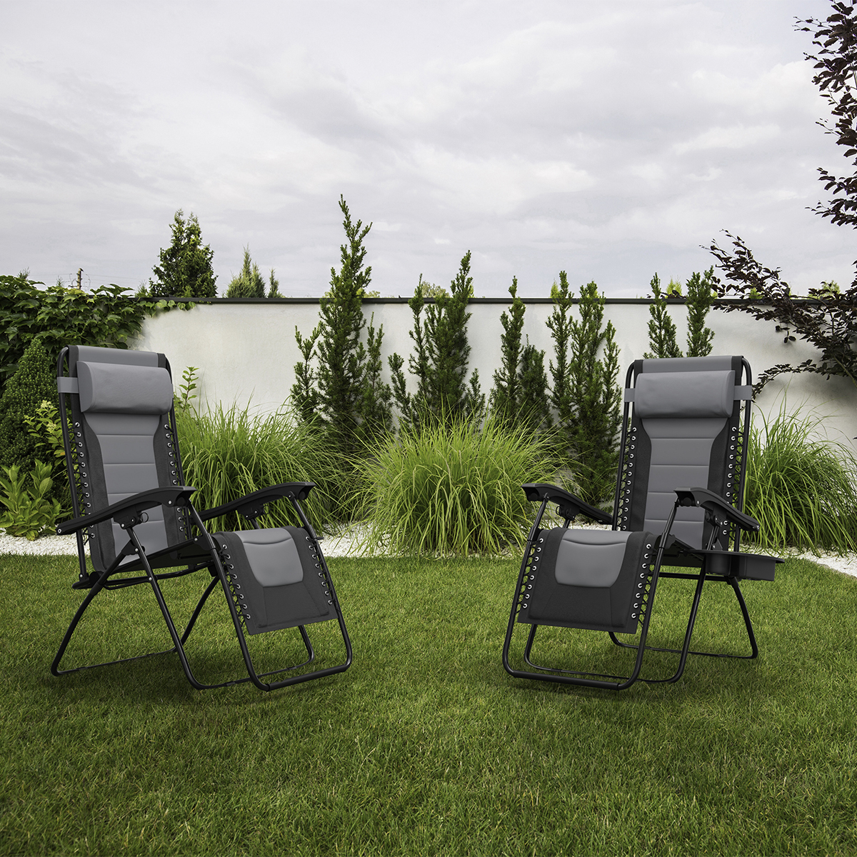 Twee grijze zero gravity stoelen op groen gazon met witte muur en planten.