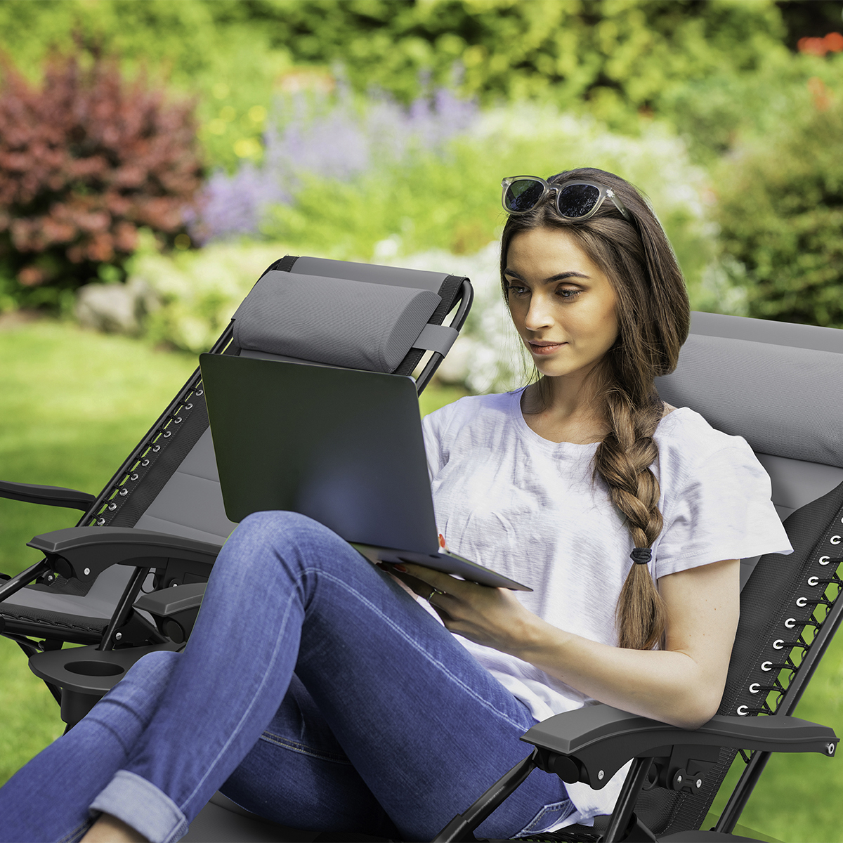 Een vrouw zit in een ligstoel in de tuin en gebruikt een laptop.