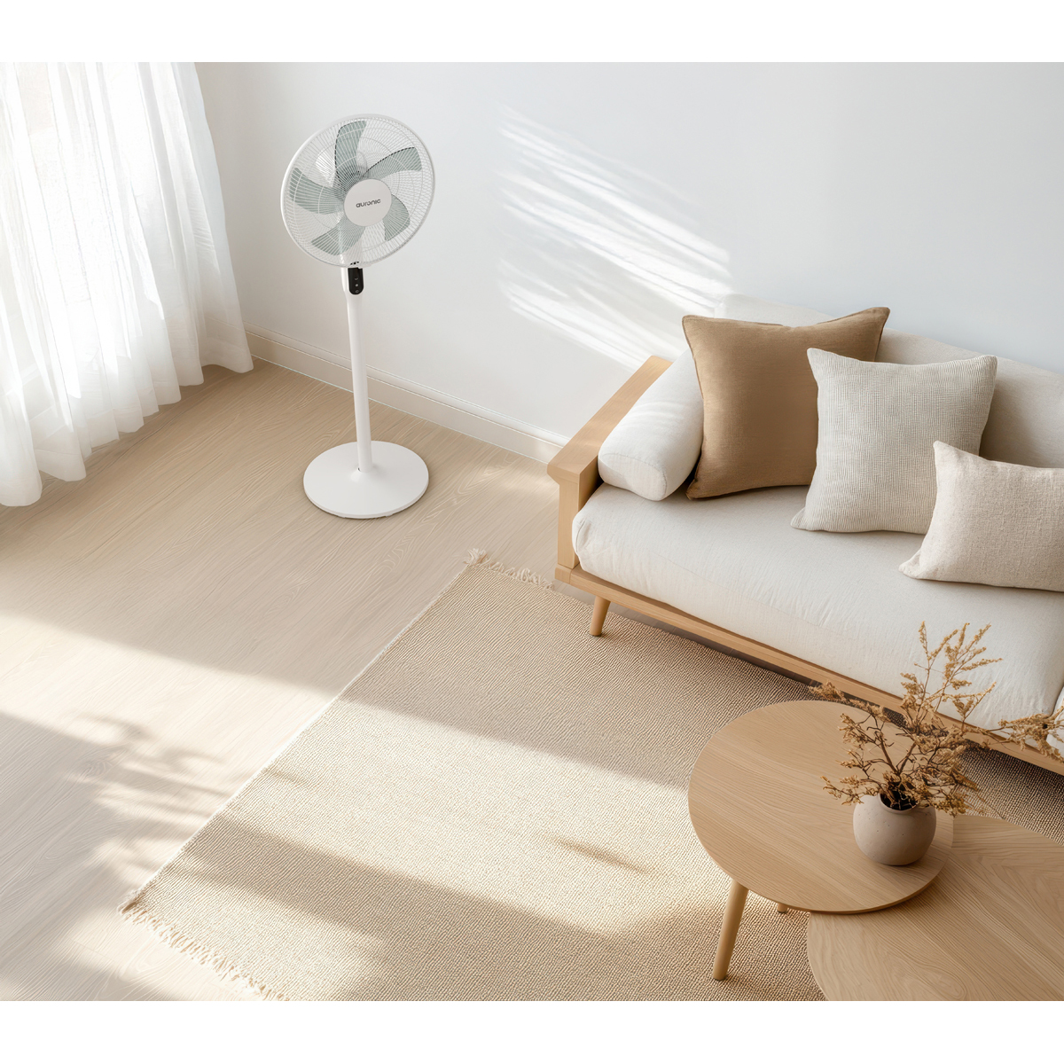 Un ventilateur blanc sur pied est à côté d'un canapé en bois clair avec des coussins beiges sur un tapis.