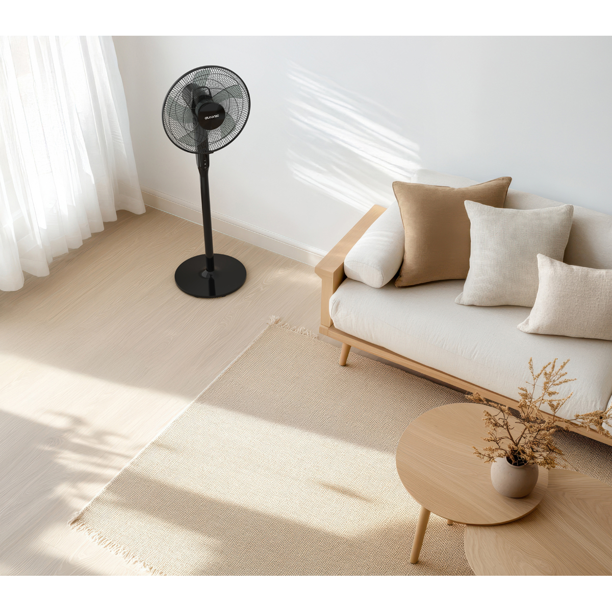 Un ventilateur sur pied noir dans un salon minimaliste avec canapé et tapis clairs.