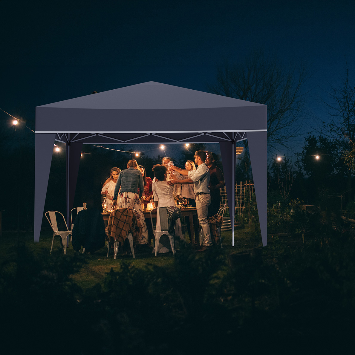 People gathered under a dark blue canopy at night, toasting drinks around a table.
