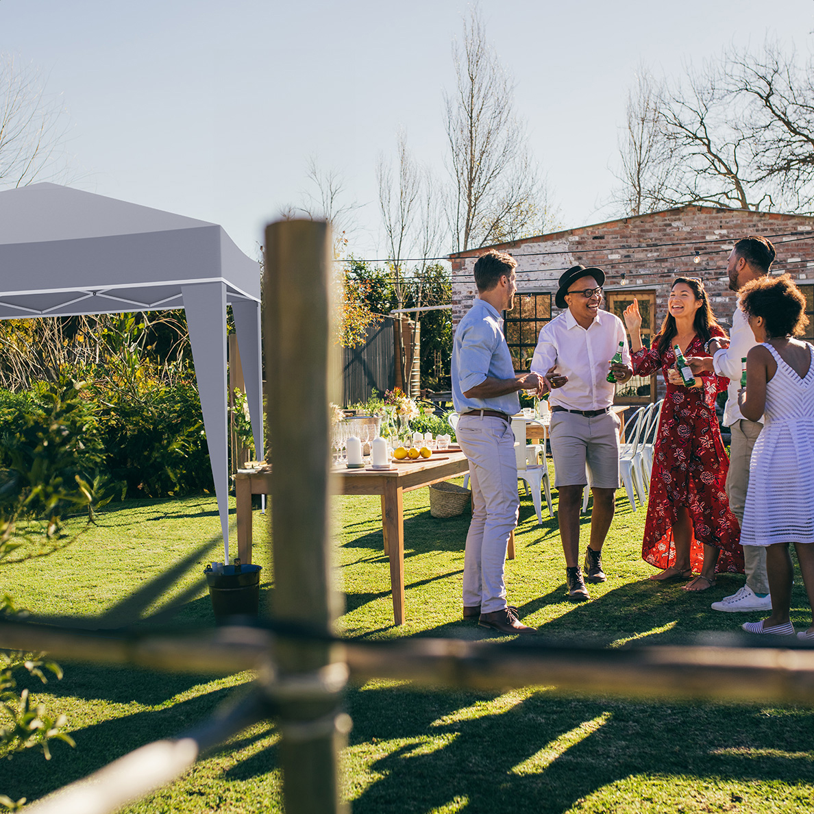 People celebrating in a garden under a gazebo, with tables and chairs.