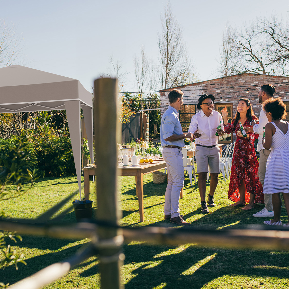 Des gens socialisent lors d'une fête dans le jardin sous un gazebo avec tables.