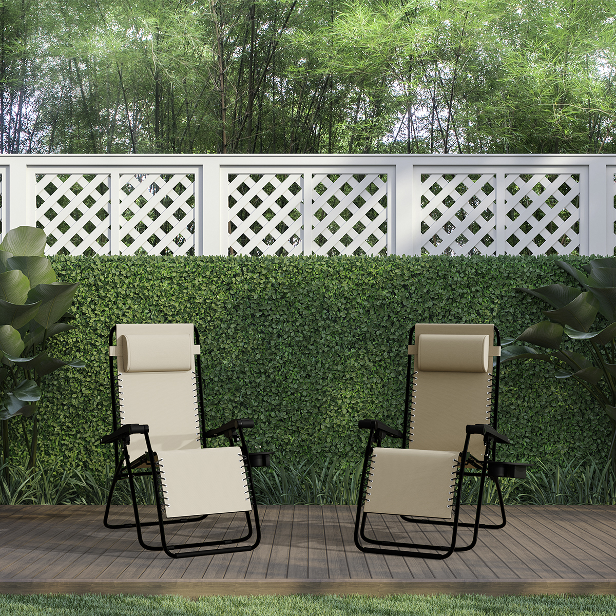 Twee beige ligstoelen op een houten terras, voor een groene heg en hek.