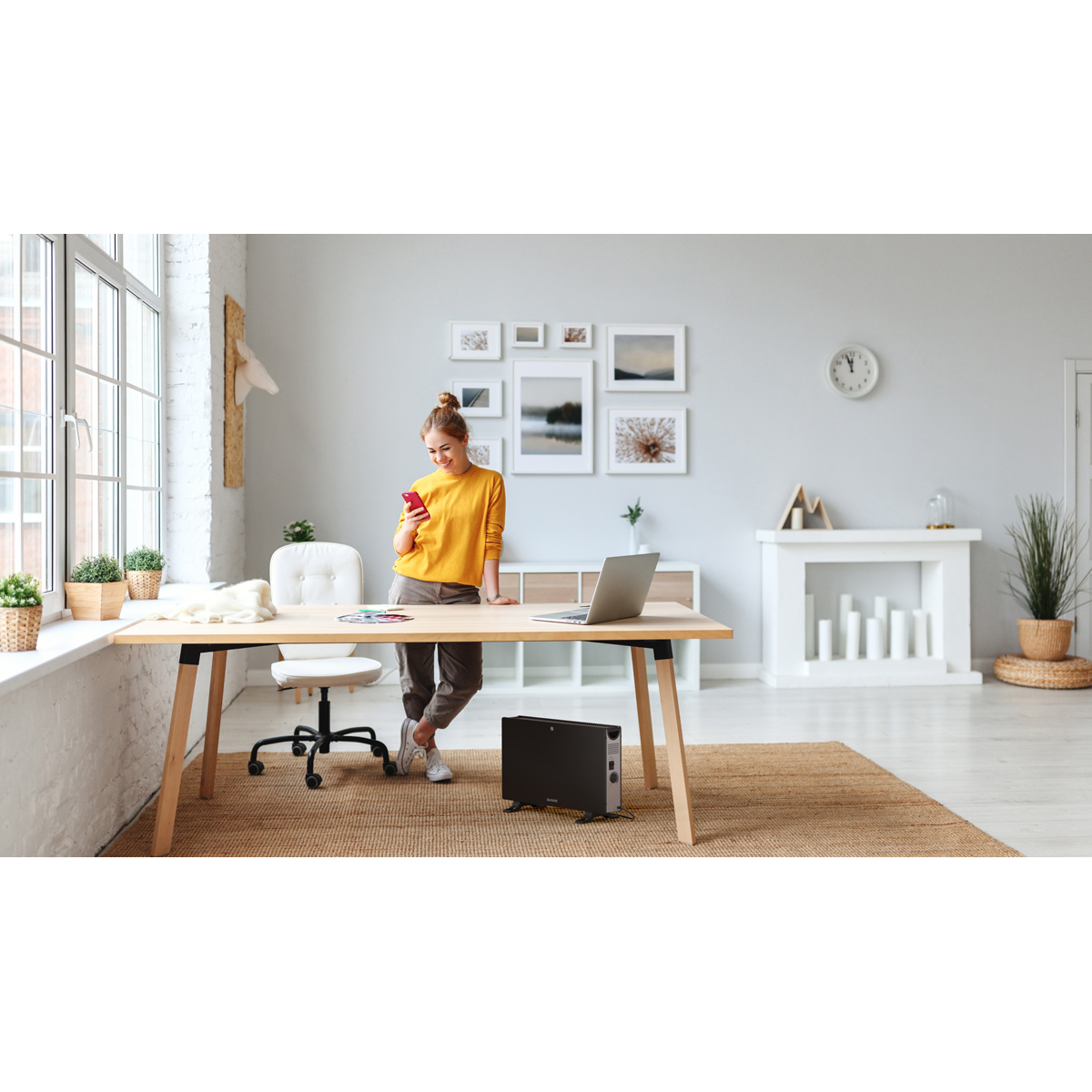 A woman in a yellow sweater stands at a desk, looking at her phone.