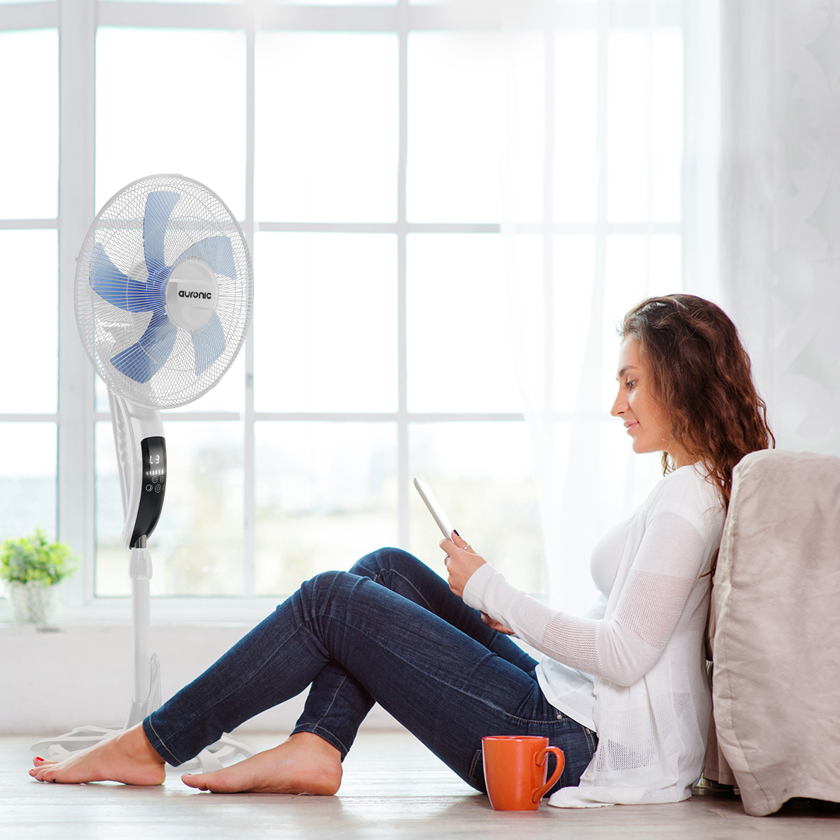 Une femme assise par terre devant un ventilateur utilise une tablette.