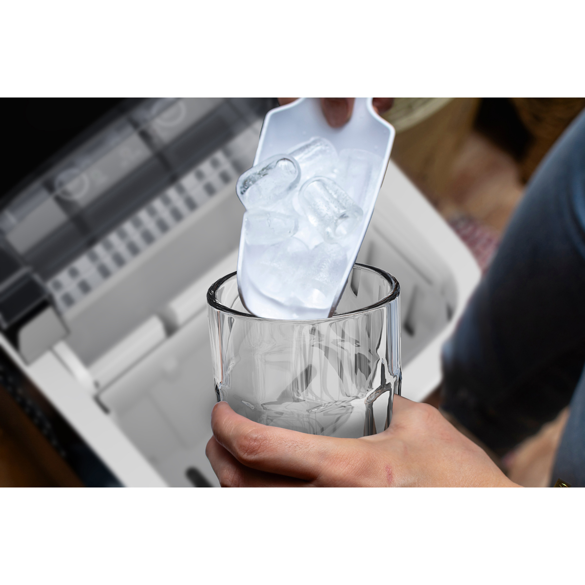 A hand scoops ice from a machine into a glass.