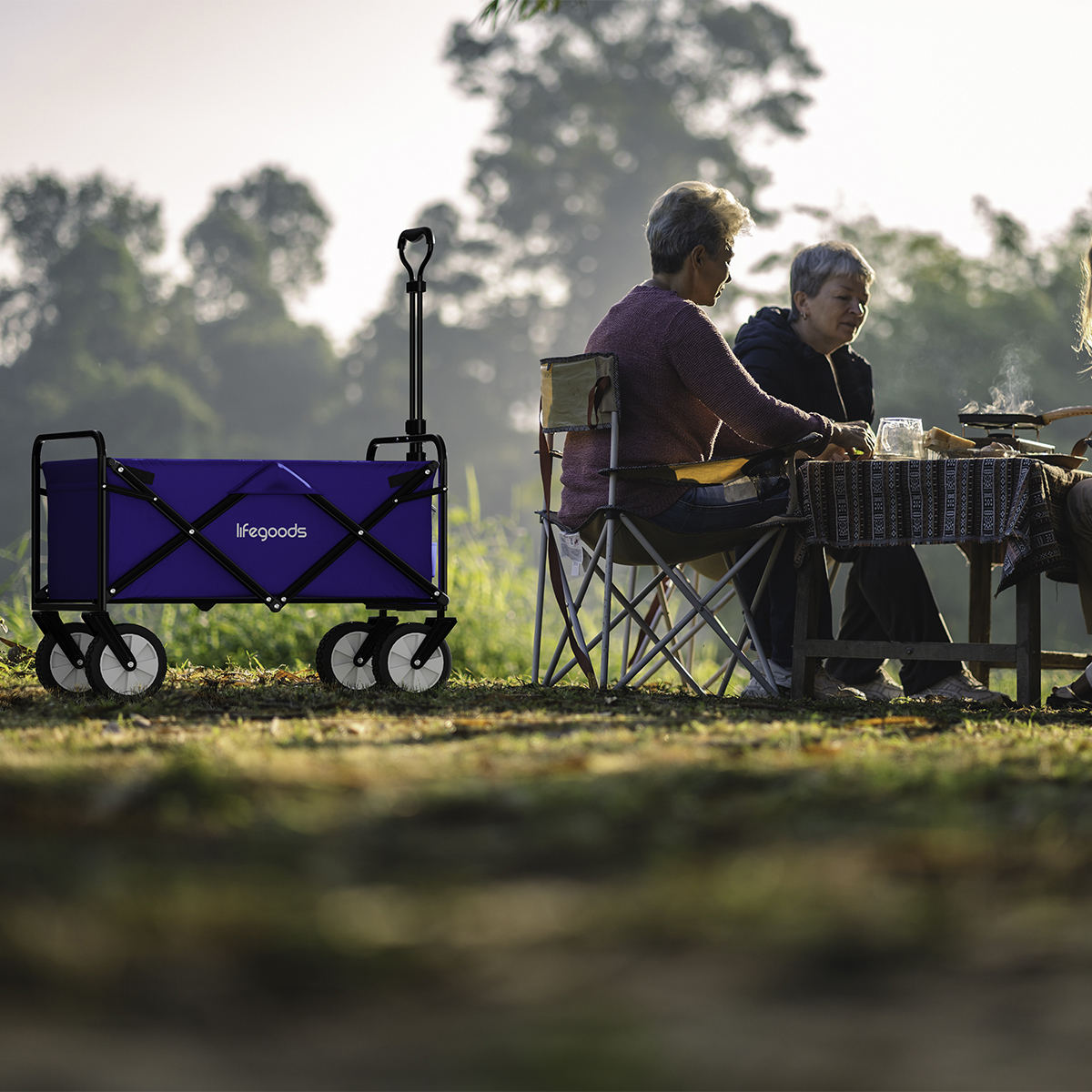 A blue wagon sits next to a group of people sitting at a table outdoors.