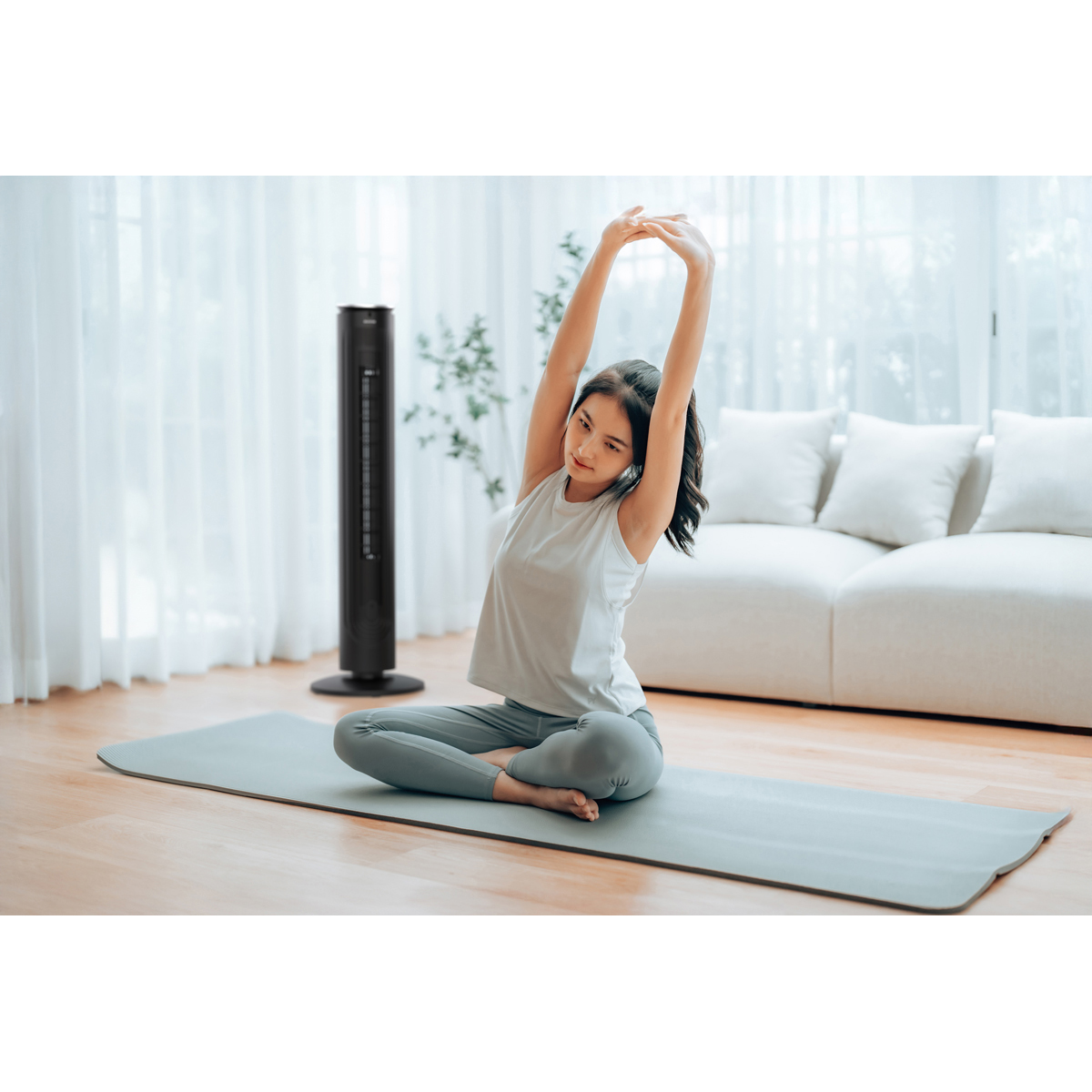 Junge Frau dehnt sich auf einer Yogamatte im Wohnzimmer mit Turmventilator.