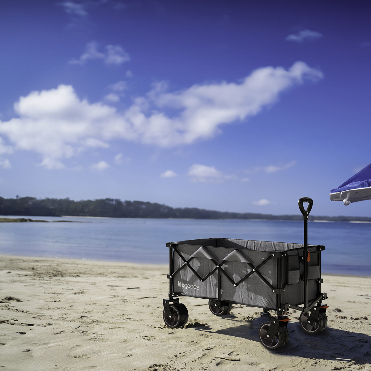 A grey wagon with a handle stands on a sandy beach next to the sea.