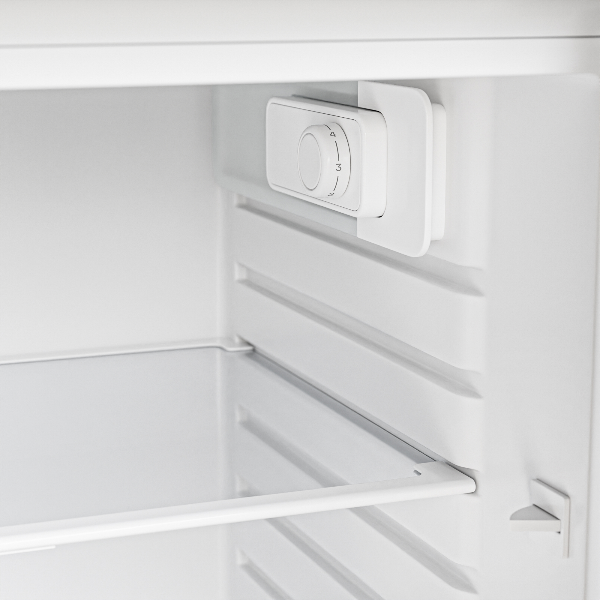 Intérieur de réfrigérateur blanc avec un bouton de réglage de température et des étagères.