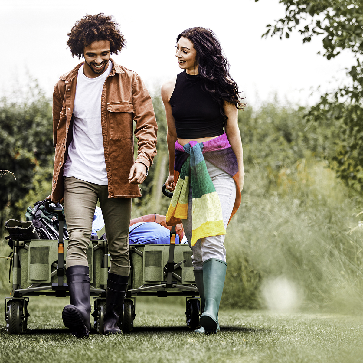 A man and a woman walk with a green wagon full of gear.