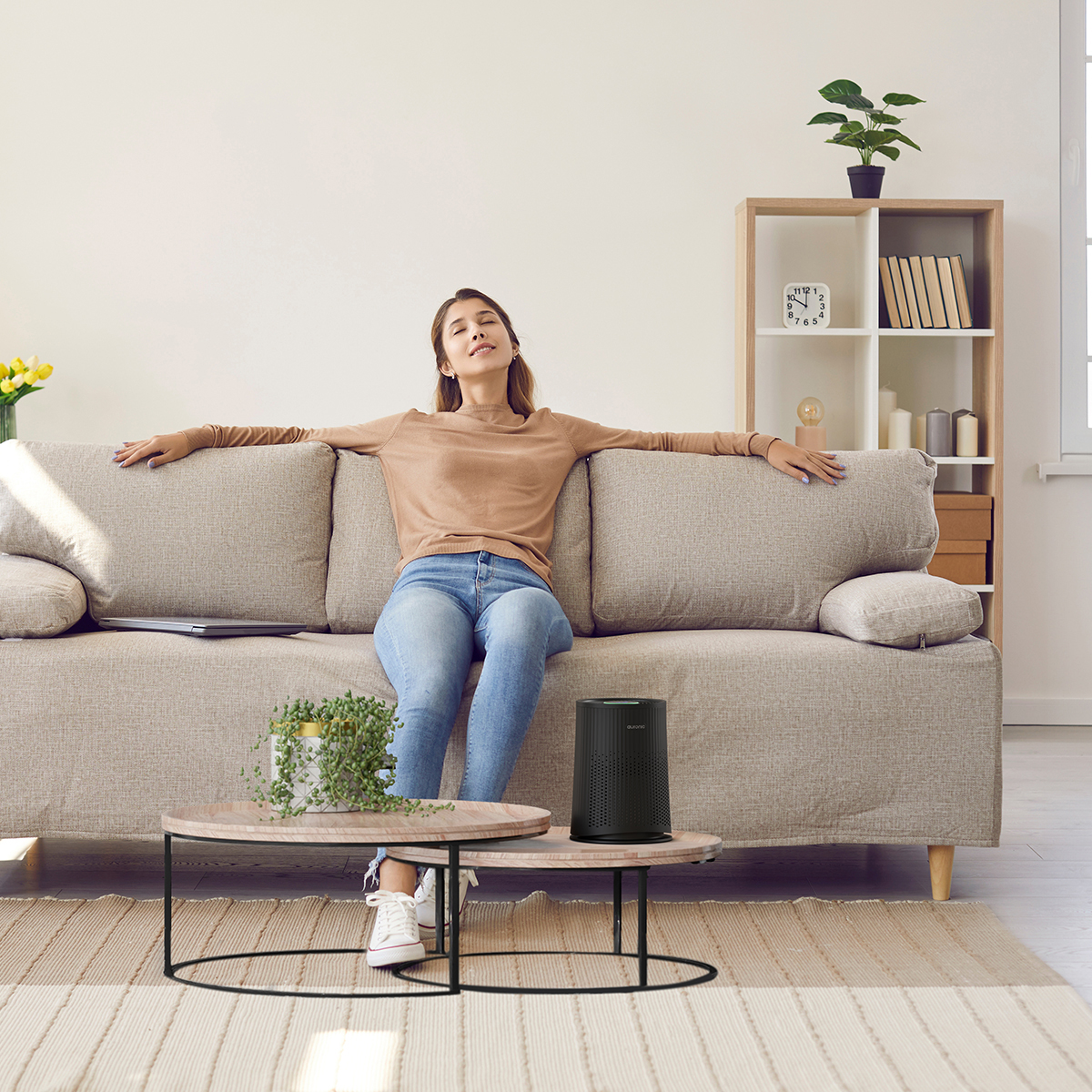 Woman relaxing on sofa with arms outstretched. Air purifier on coffee table.