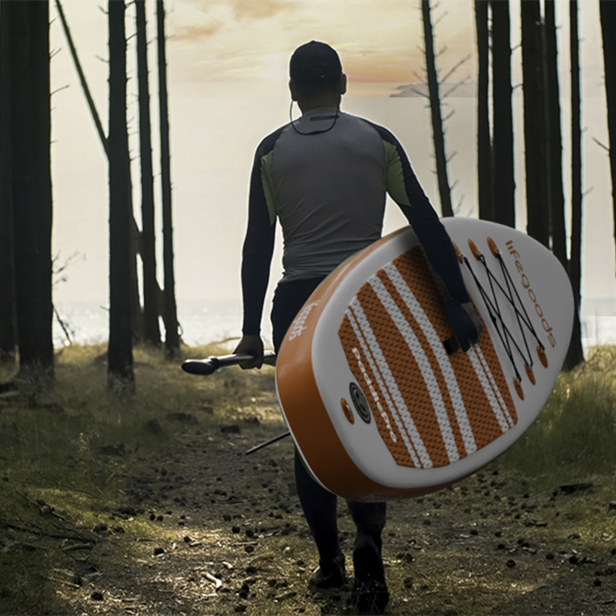 Man met paddleboard loopt door bomen naar de oceaan bij zonsondergang.