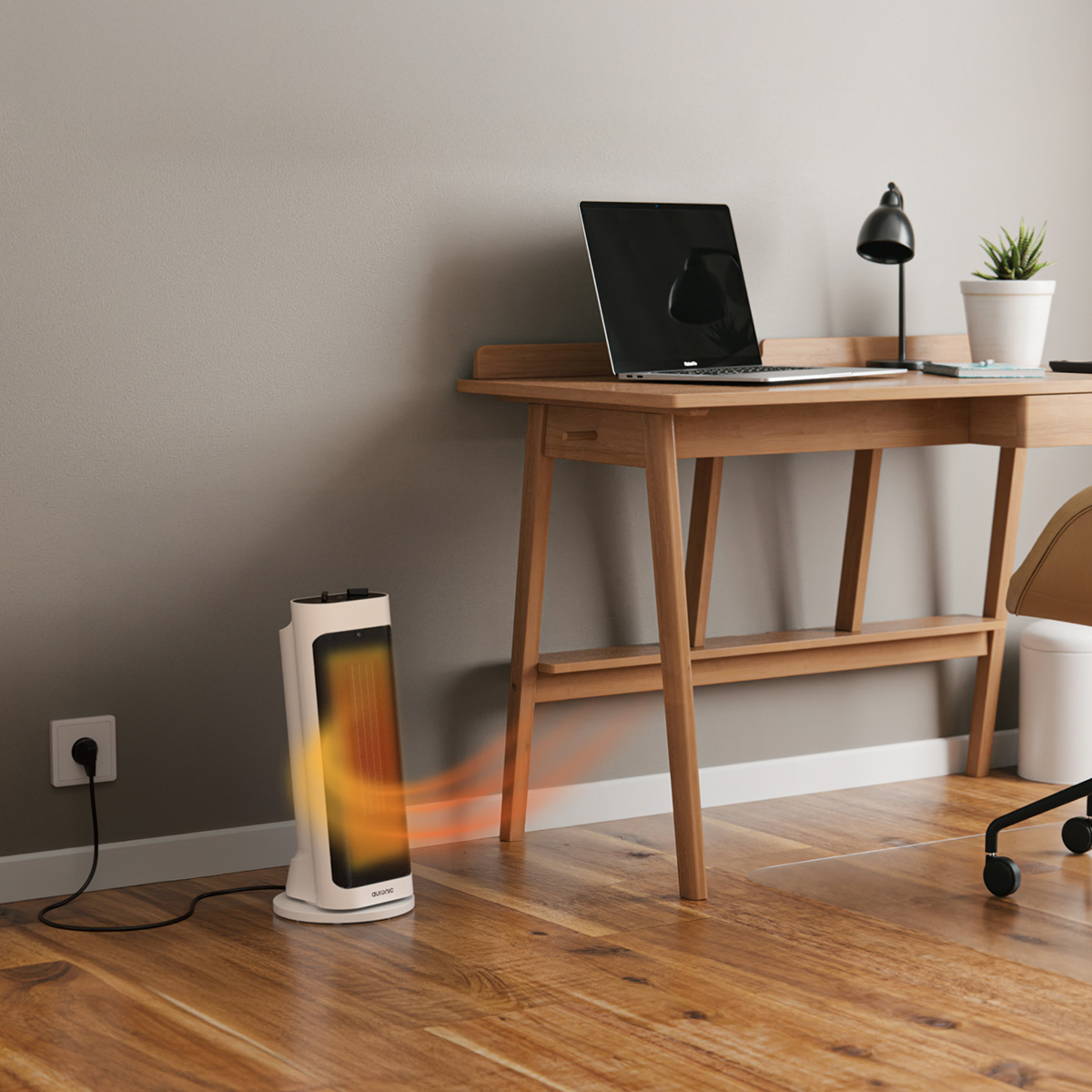 A white oscillating heater blows warm air next to a wooden desk with a laptop.
