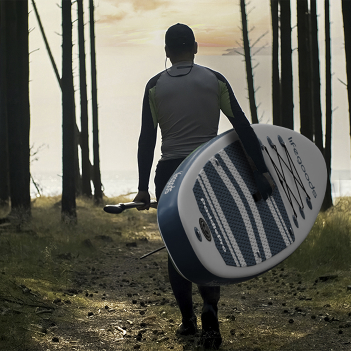 Man met paddleboard en peddel loopt door een bos naar het water.