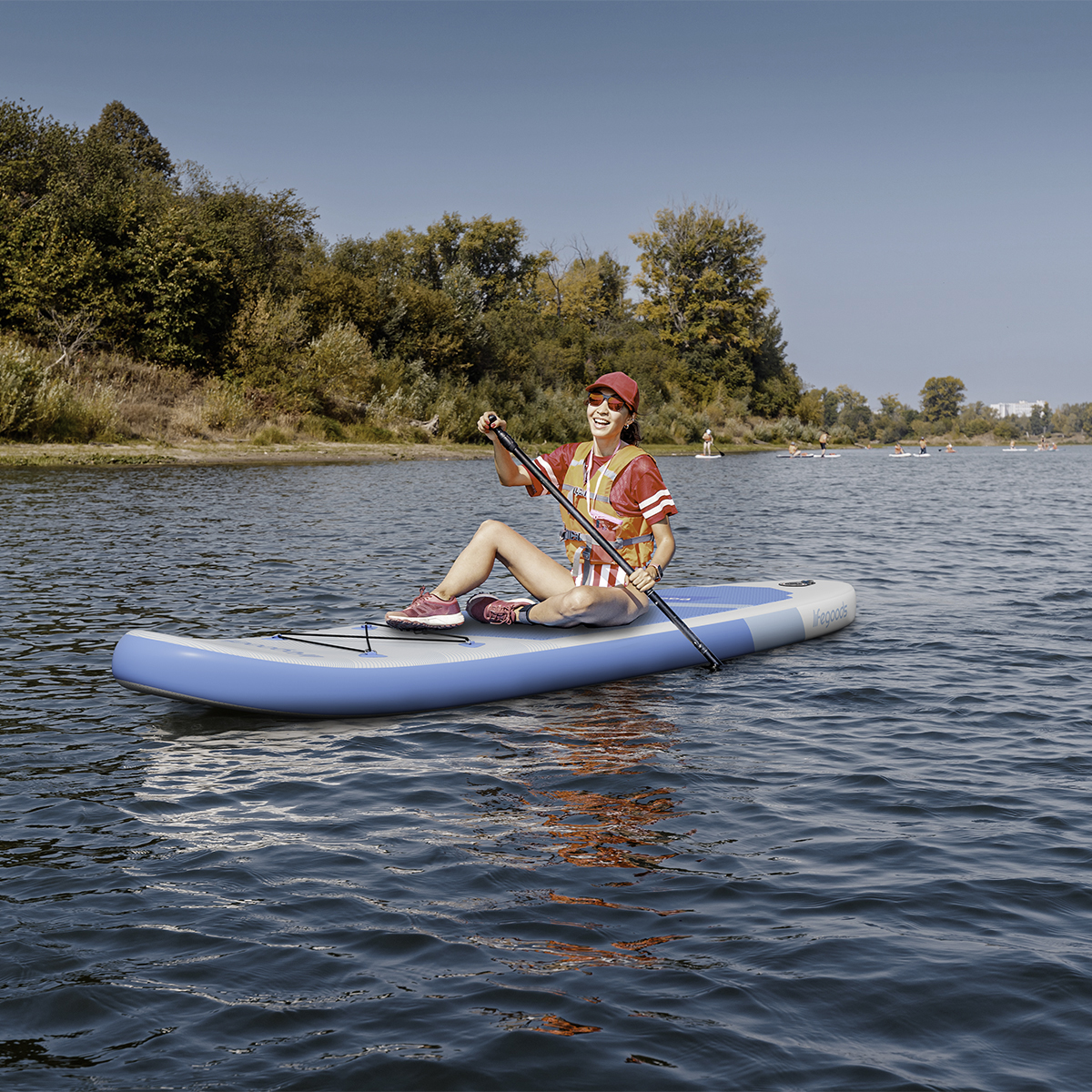 Eine Frau auf einem Stand-Up-Paddleboard auf einem See, mit Bäumen im Hintergrund.