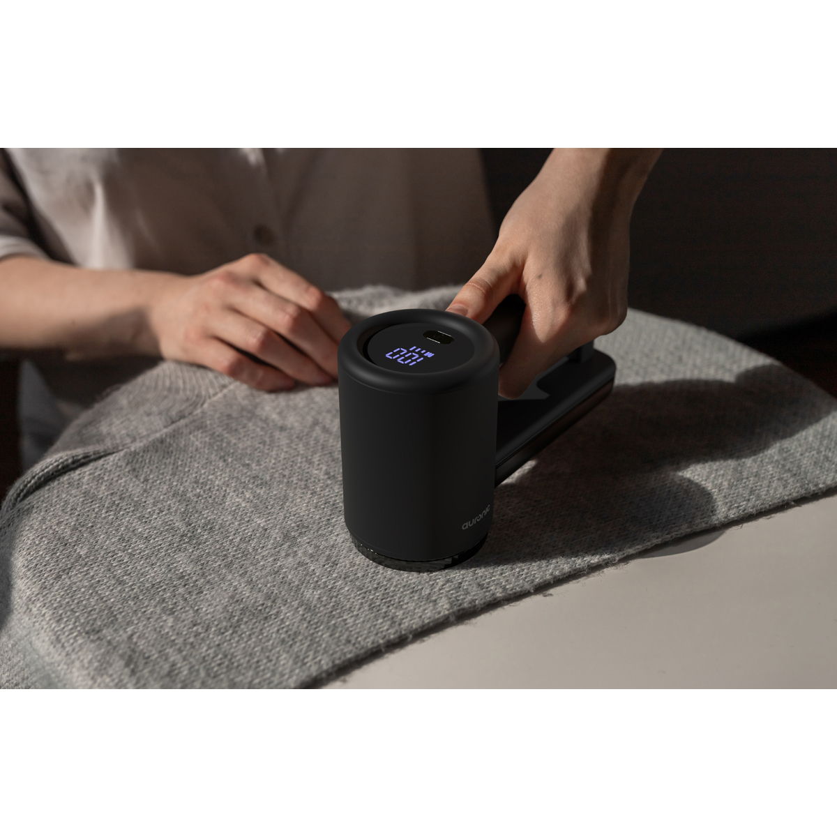 Un rasoir à tissu noir avec écran numérique est utilisé sur une couverture tricotée grise.