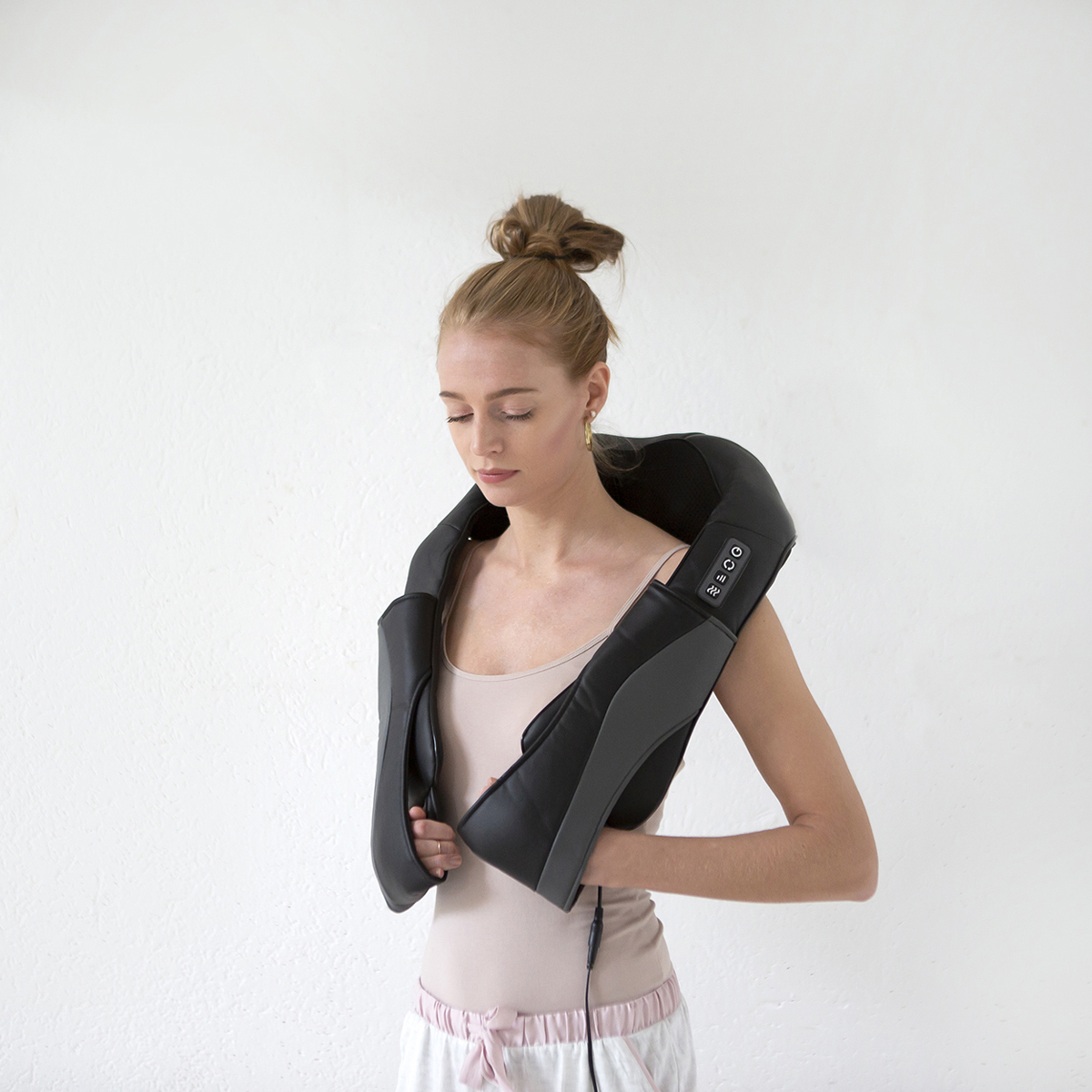 A woman wearing a neck massager around her neck against a white wall.