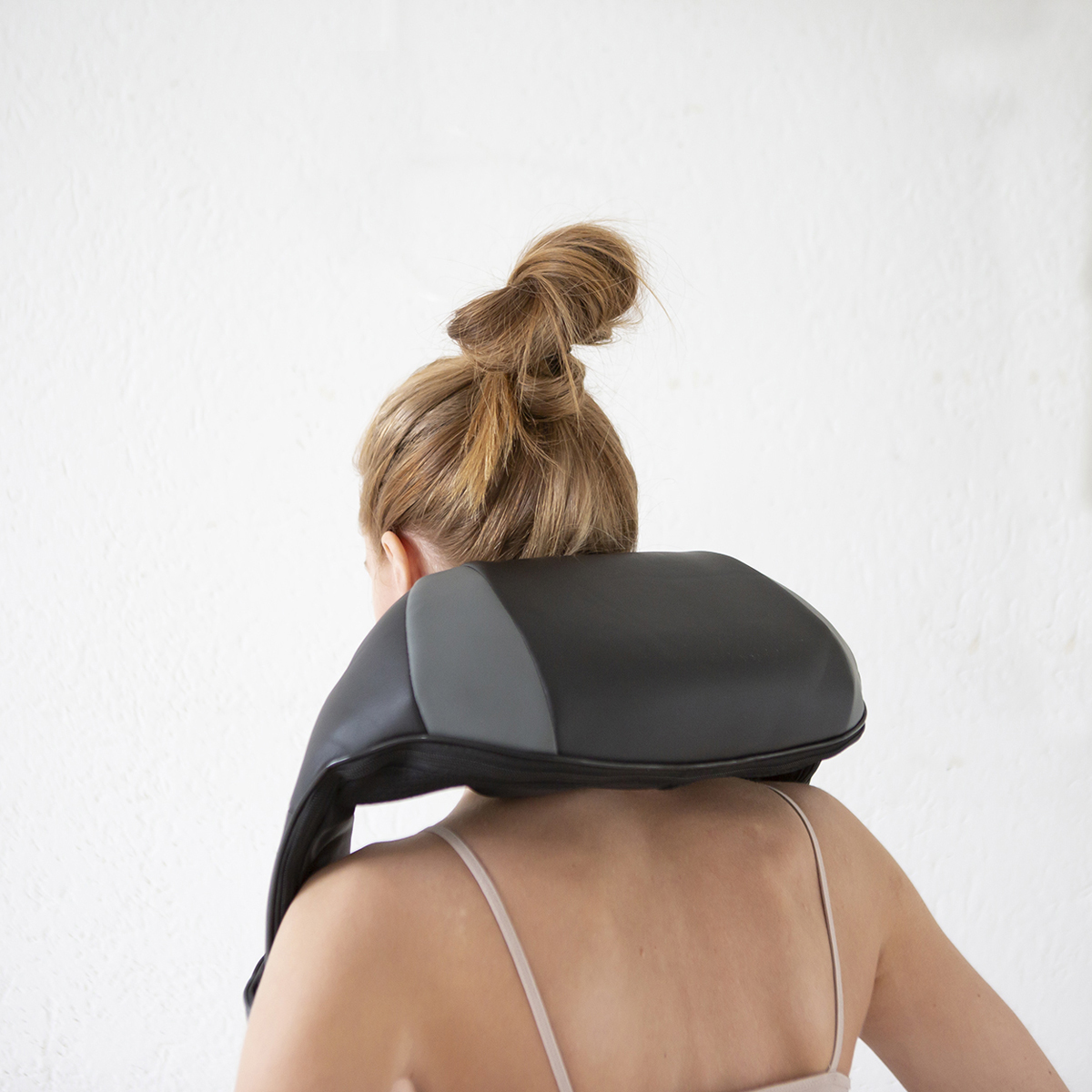 Woman with a neck massager, blonde hair in a bun.