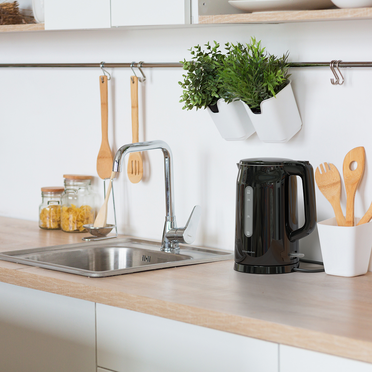 Een keuken met gootsteen, waterkoker, houten keukengerei en planten.