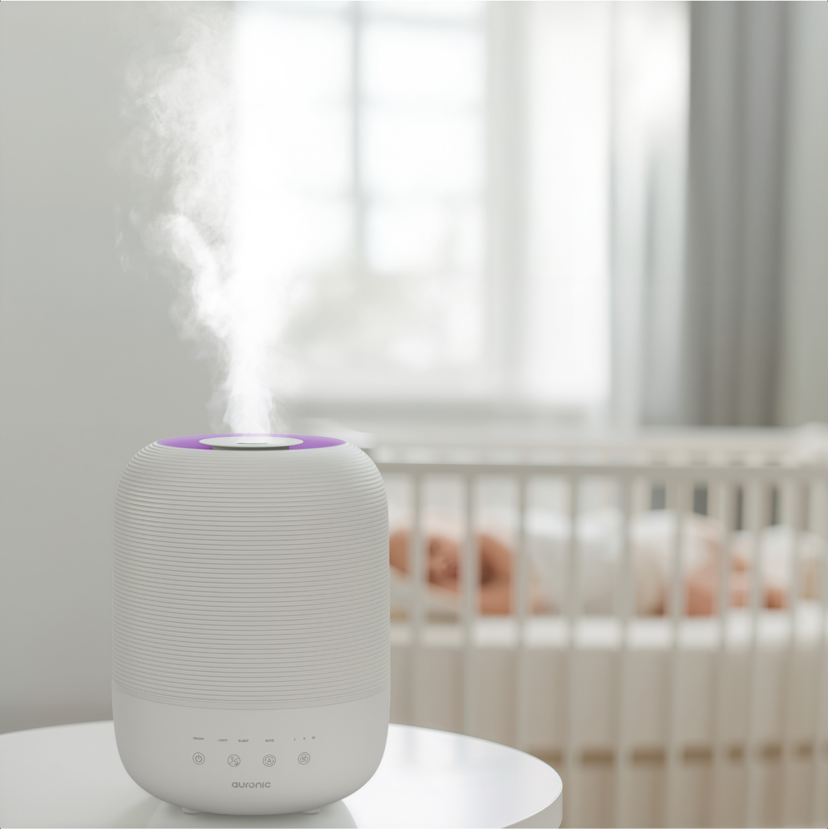 A white humidifier with purple accent emits mist; a baby sleeps in a crib in the background.
