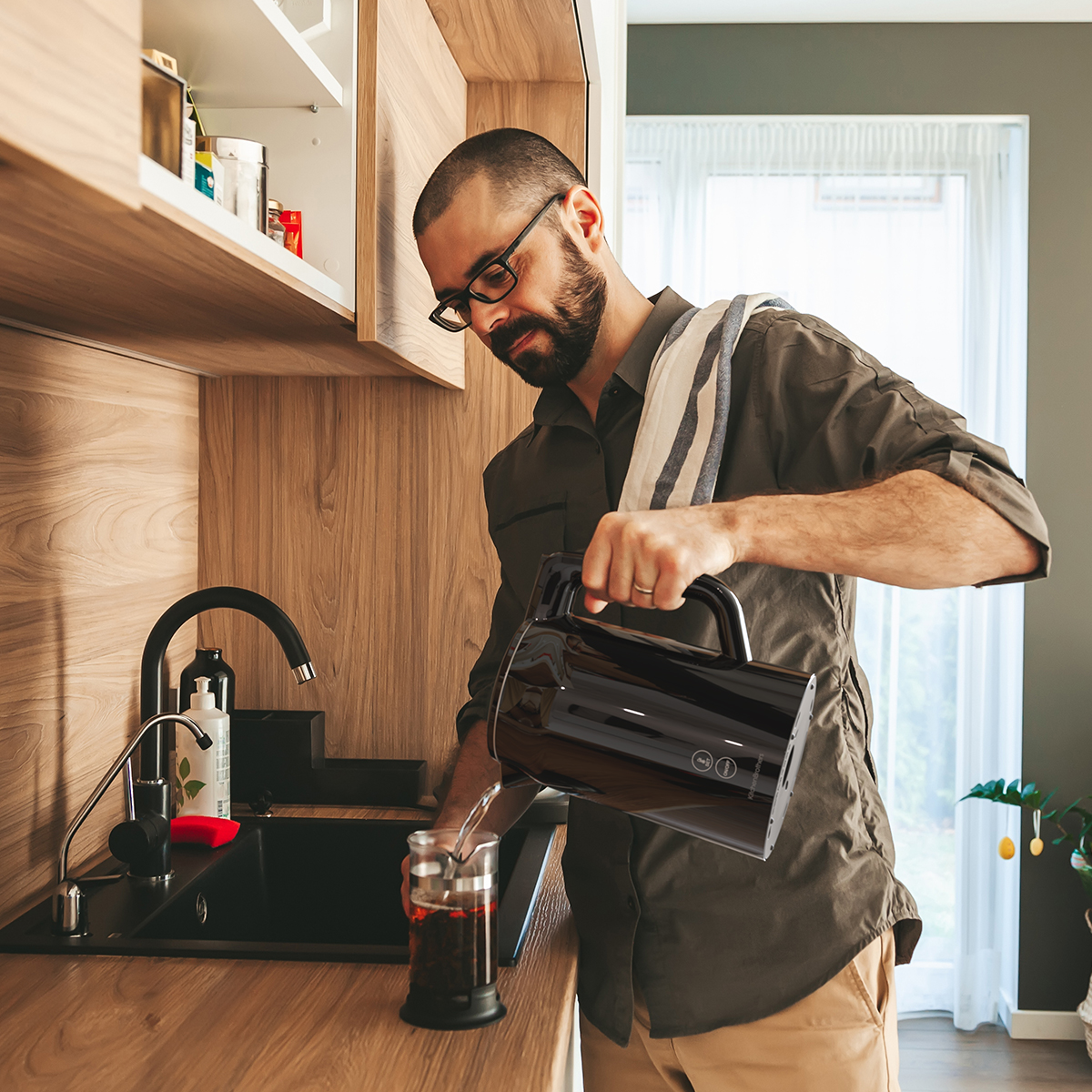 Man met bril schenkt water uit zwarte waterkoker in cafetière.