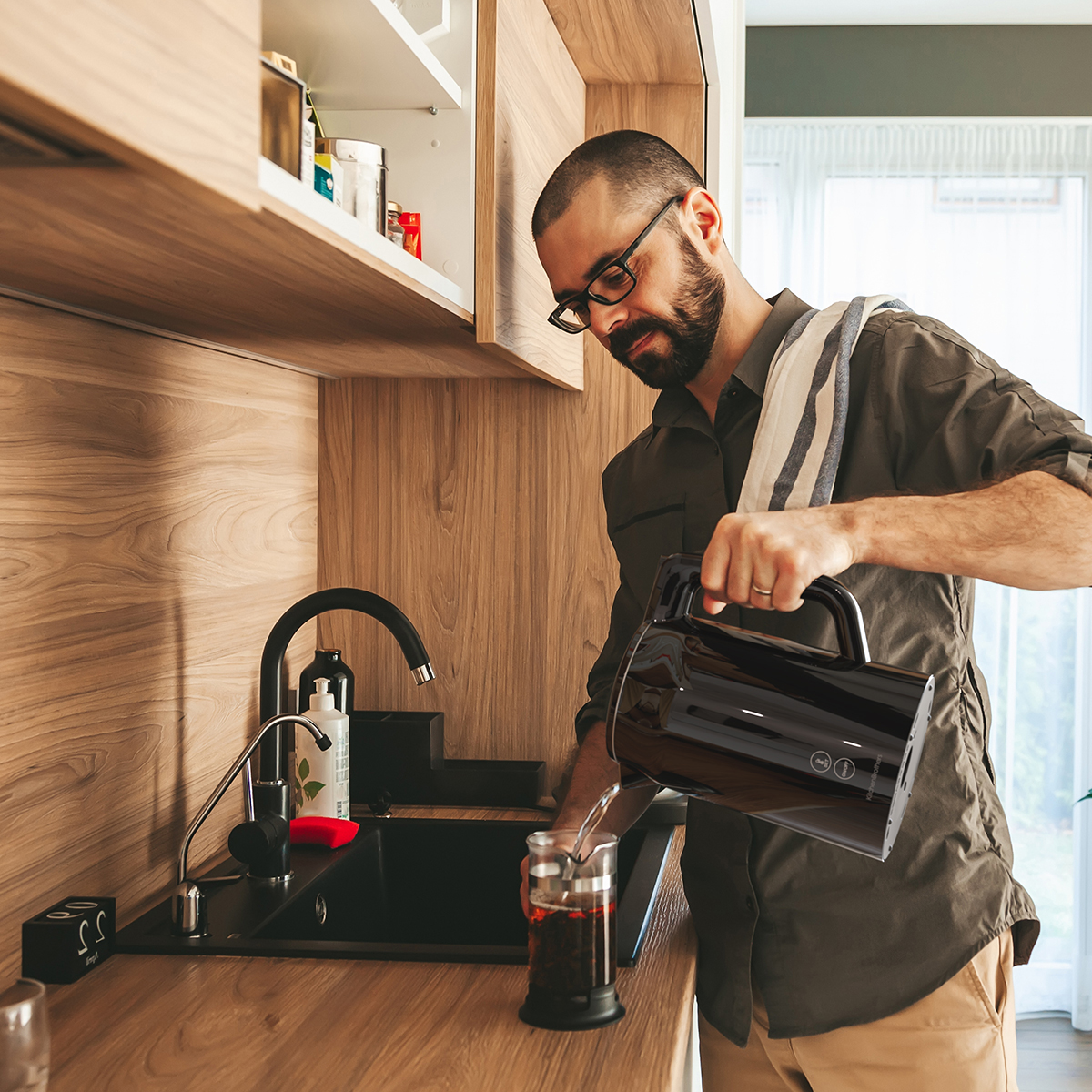 Man schenkt water uit zwarte waterkoker in cafetière in een keuken.