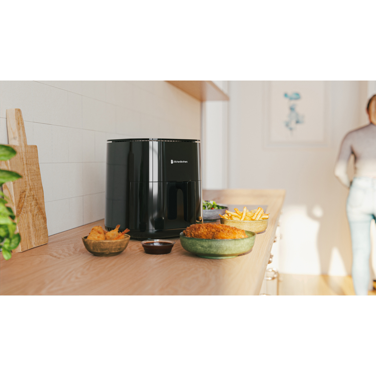 A black air fryer sits on a wooden counter with bowls of fried shrimp, fries, and salad.