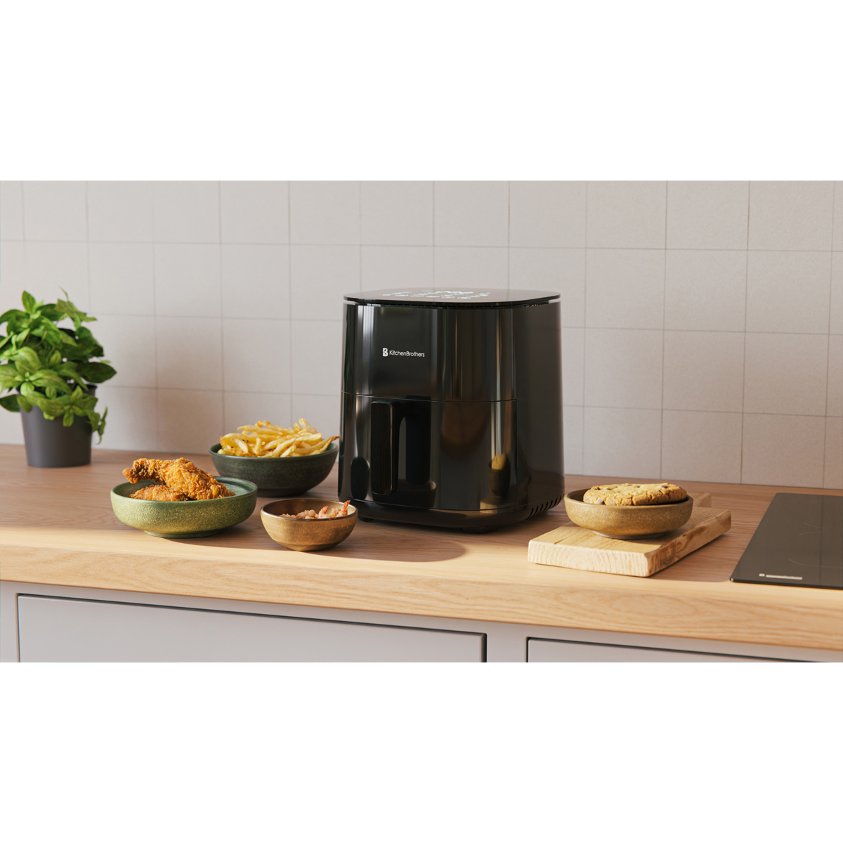 Black air fryer with sides like fries, chicken, and a cookie on a countertop.