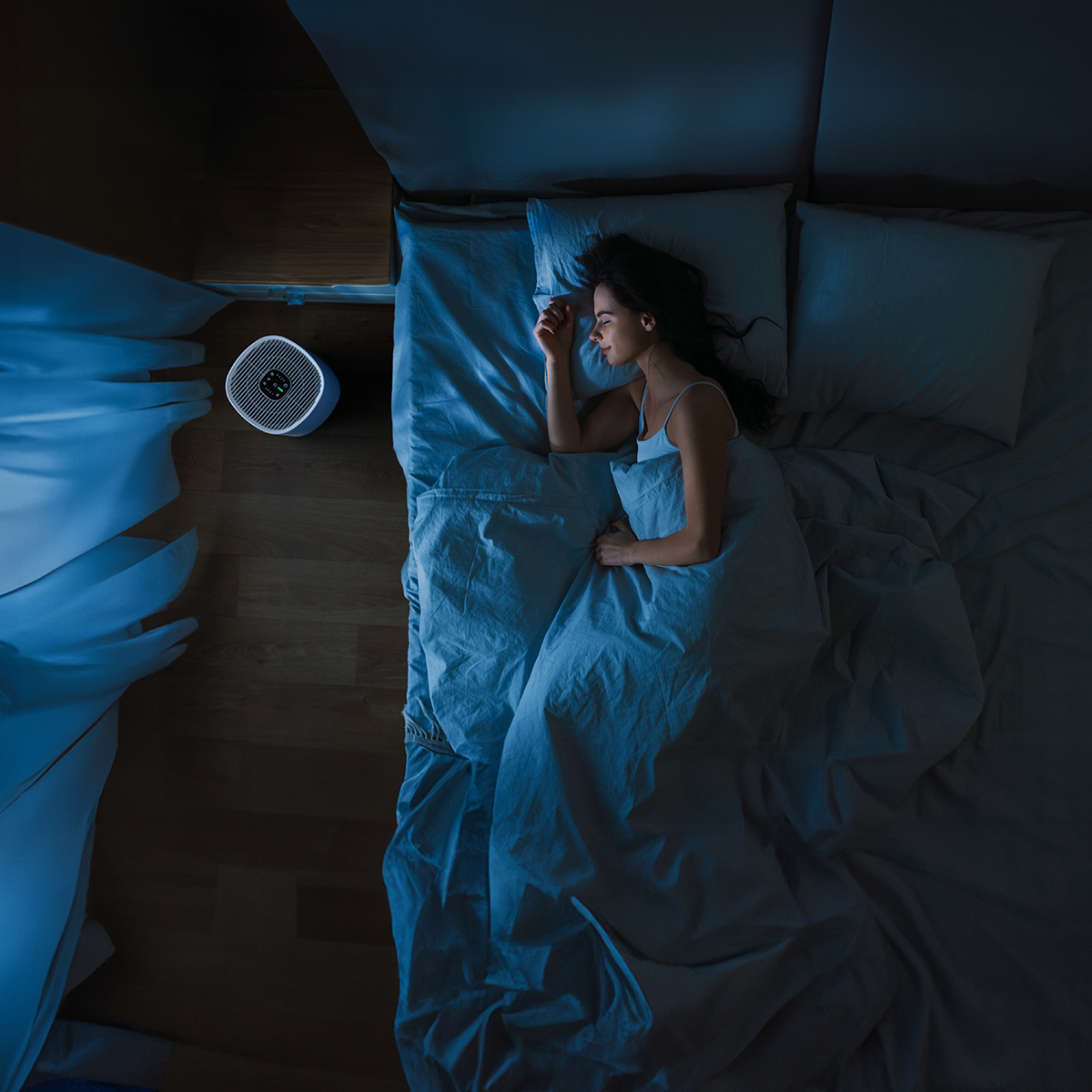 Woman sleeps in bed at night with air purifier on wooden floor.