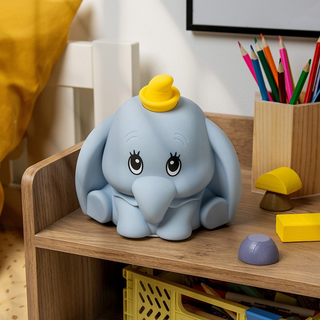 Jasnoniebieska figurka Dumbo w żółtym kapeluszu siedzi na drewnianej półce.
