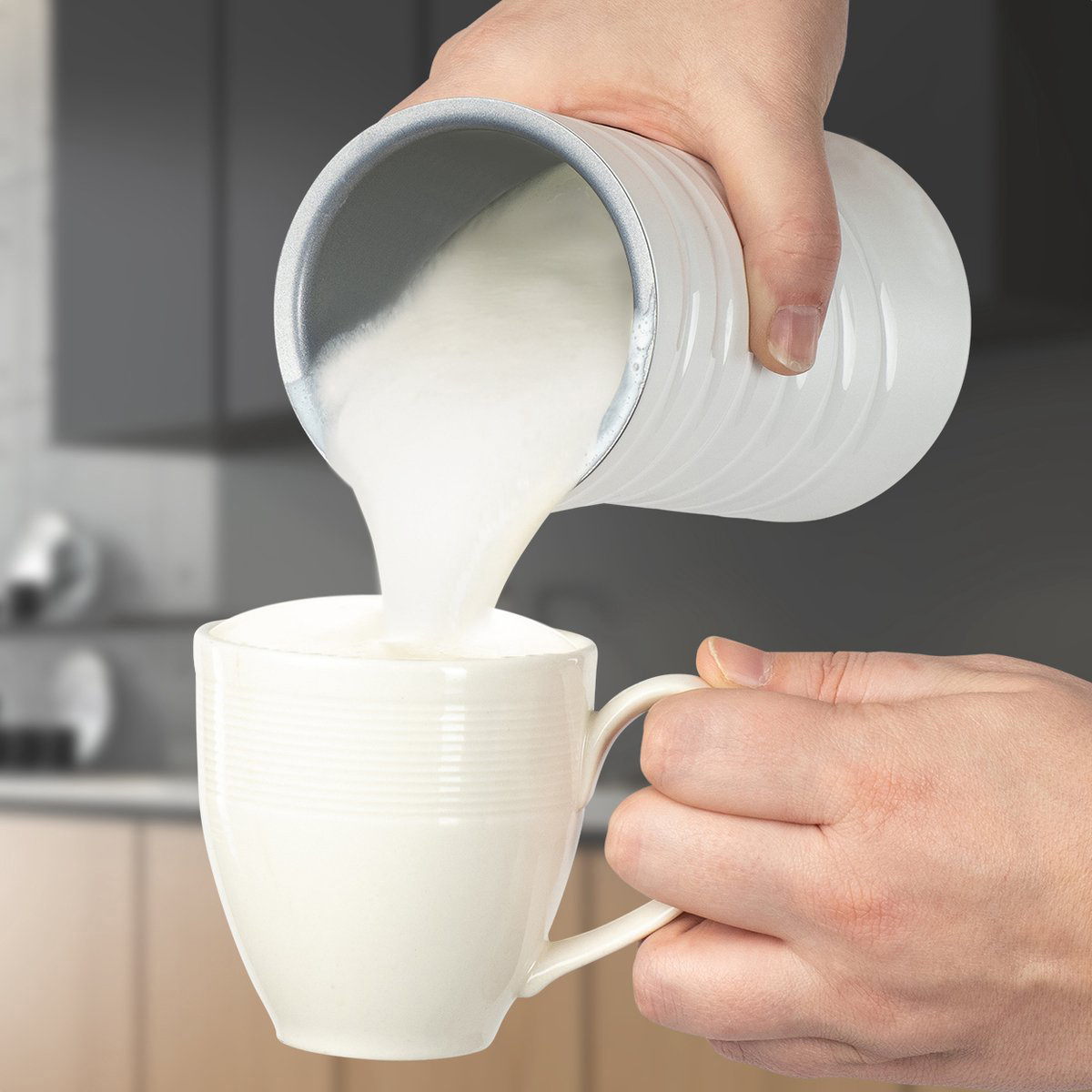 Milch wird aus einem weißen Krug in eine weiße Tasse gegossen.